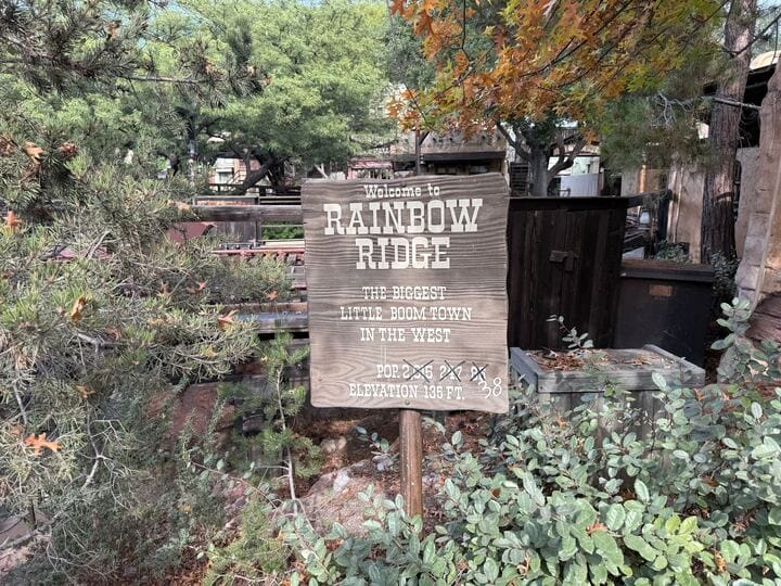 A weathered wooden sign welcomes visitors to Big Thunder Mountain Railroad at Disneyland, surrounded by greenery and lush foliage.