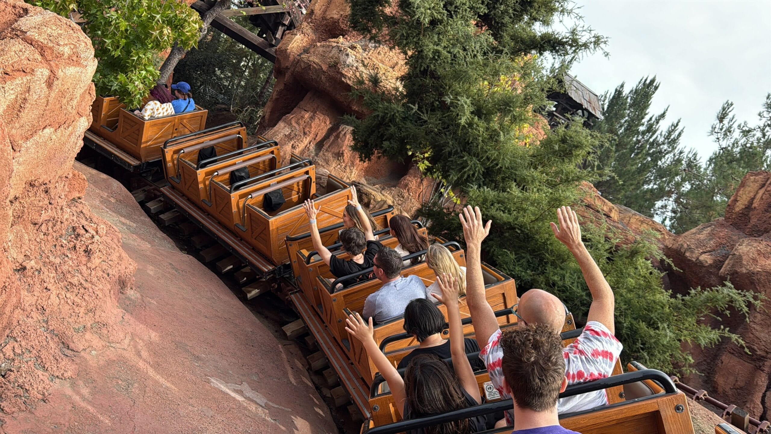 Guests speed past red rocks and trees, arms up, on Disneyland’s Big Thunder Mountain—no castle visible like those in Disney parks.
