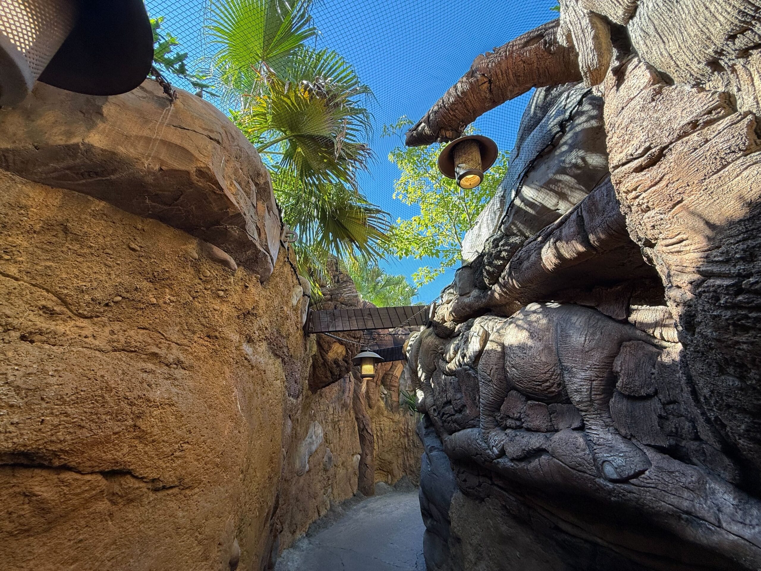 A winding rocky pathway with classic Disney park lamps, palm trees, and bright blue sky—reminiscent of Adventureland’s trails.