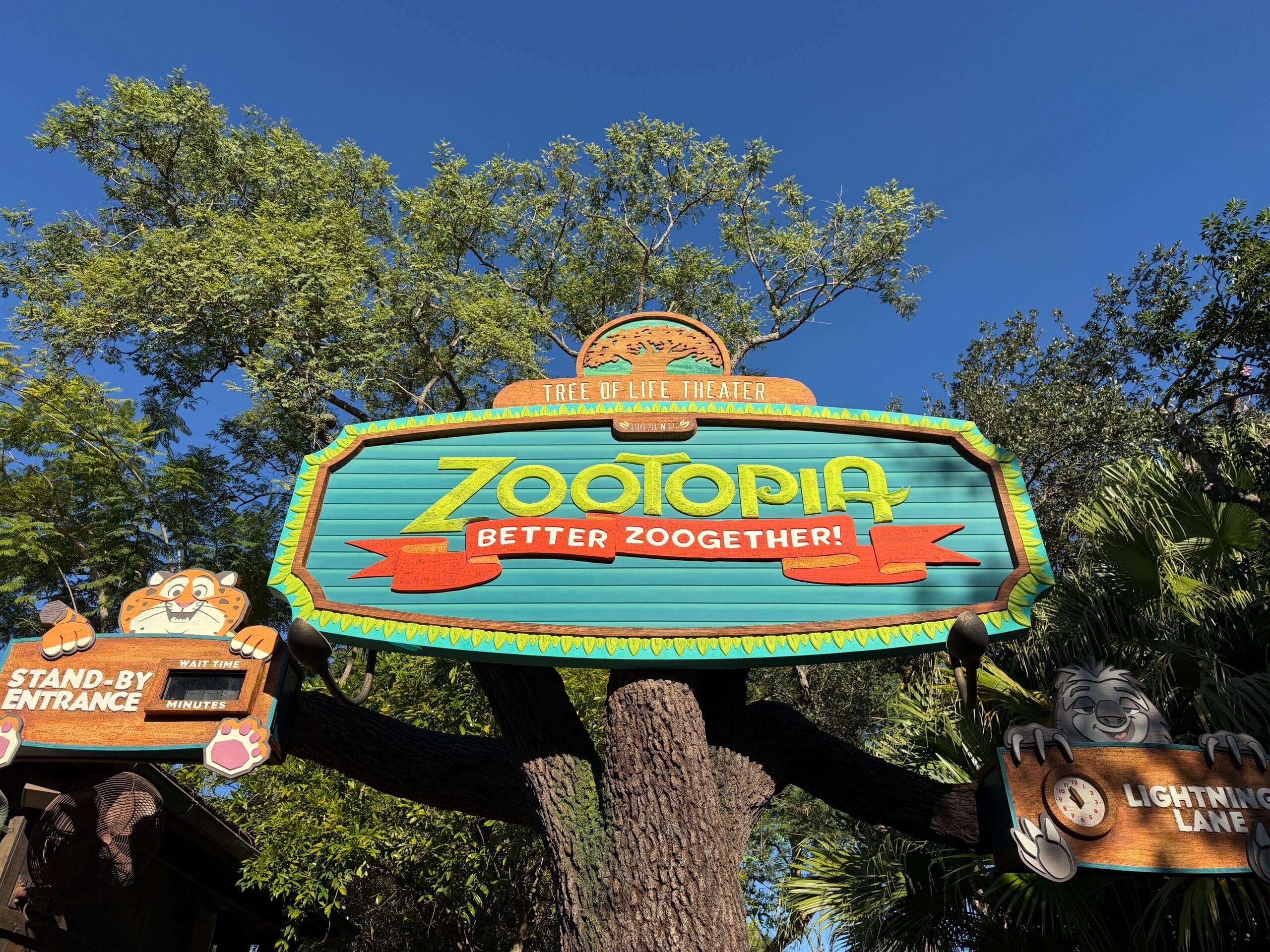 Vibrant "Zootopia: Better Zoogether!" sign near Animal Kingdom’s Tree of Life, framed by lush trees and clear blue Disney sky.