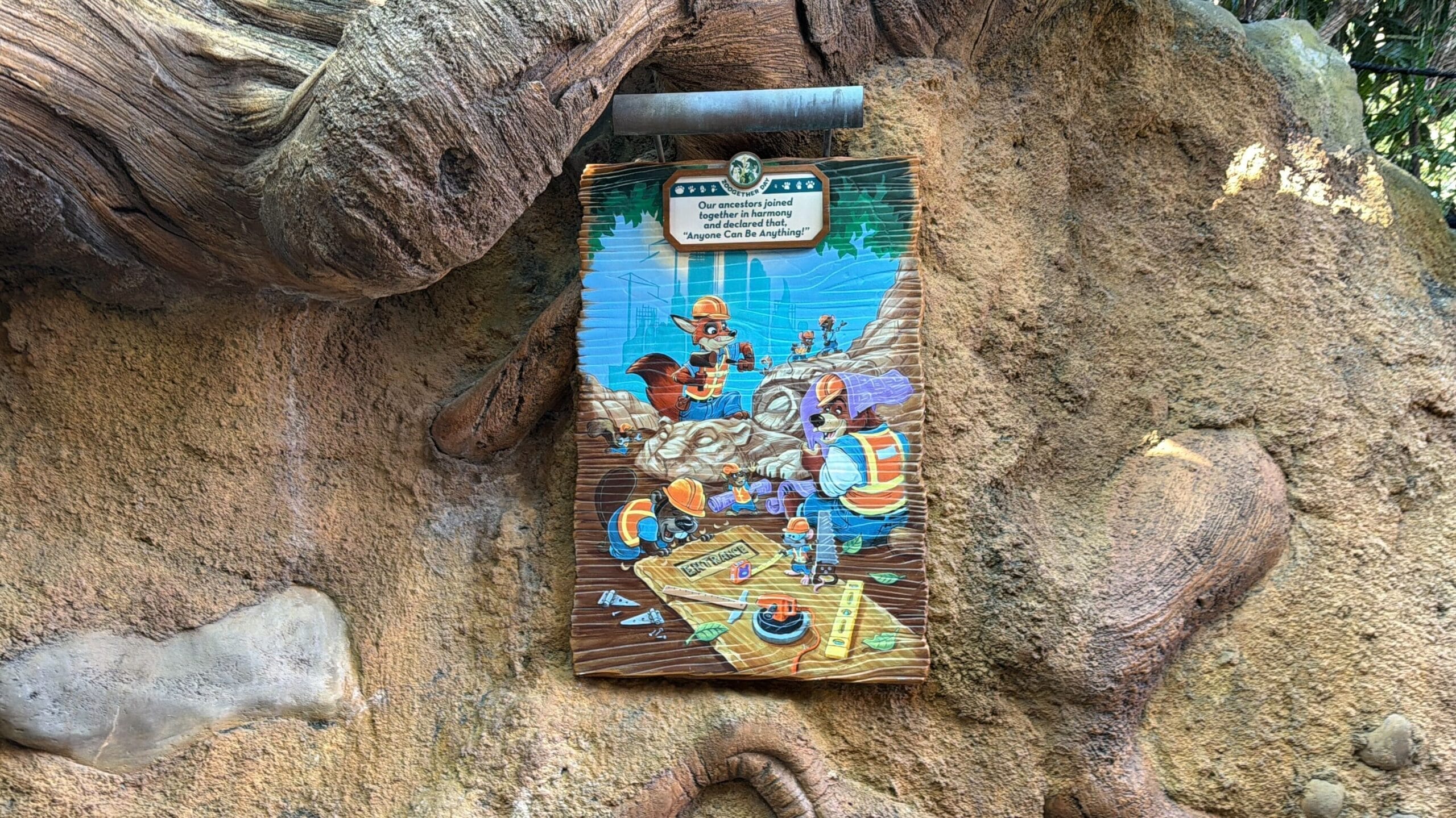 A vibrant illustrated sign on a textured wall at a Disney park features Zootopia animals planning an adventure together.