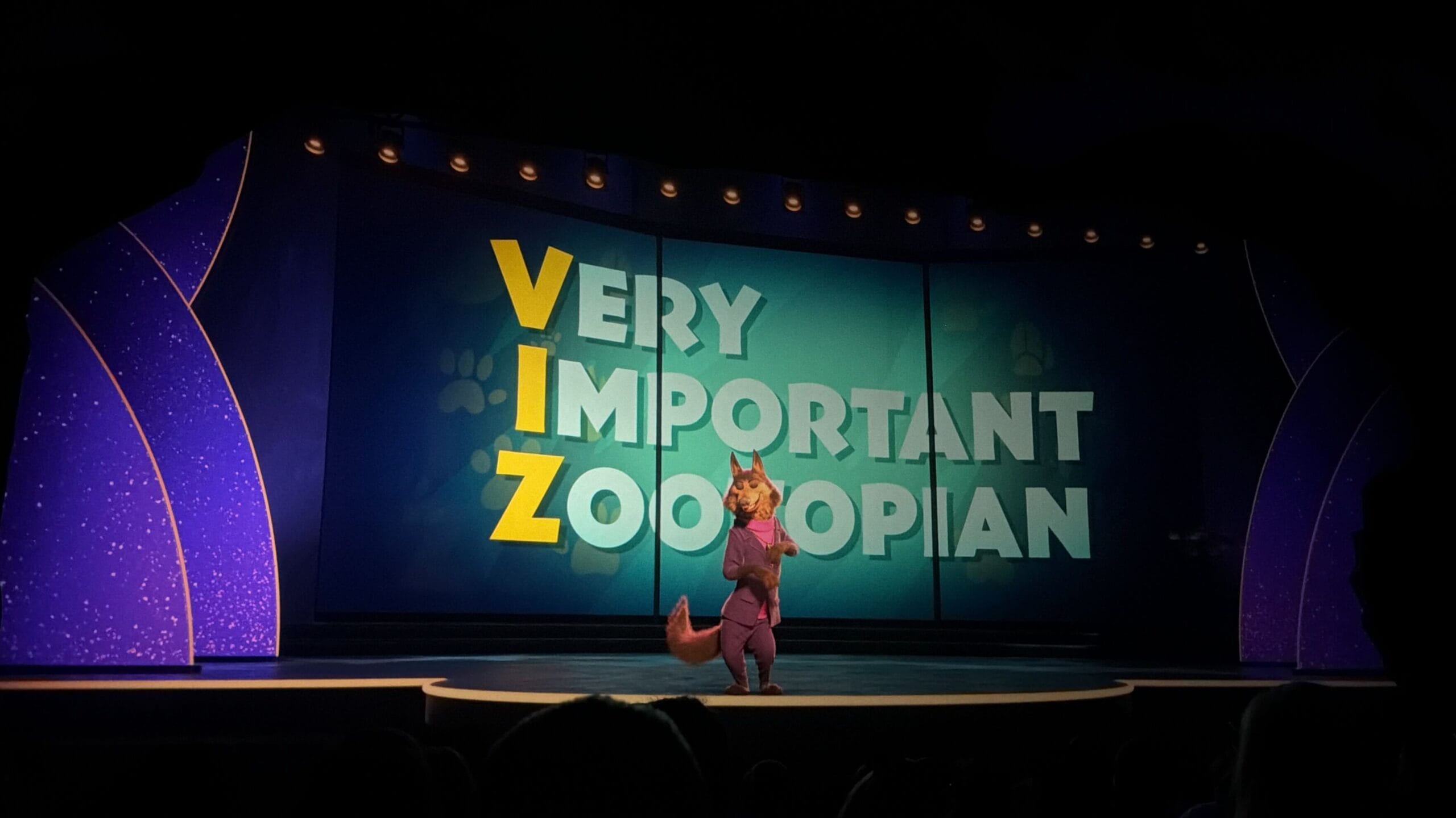 A Disney character poses on stage before a Zootopia sign at Animal Kingdom, no castle like Cinderella or Sleeping Beauty in view.