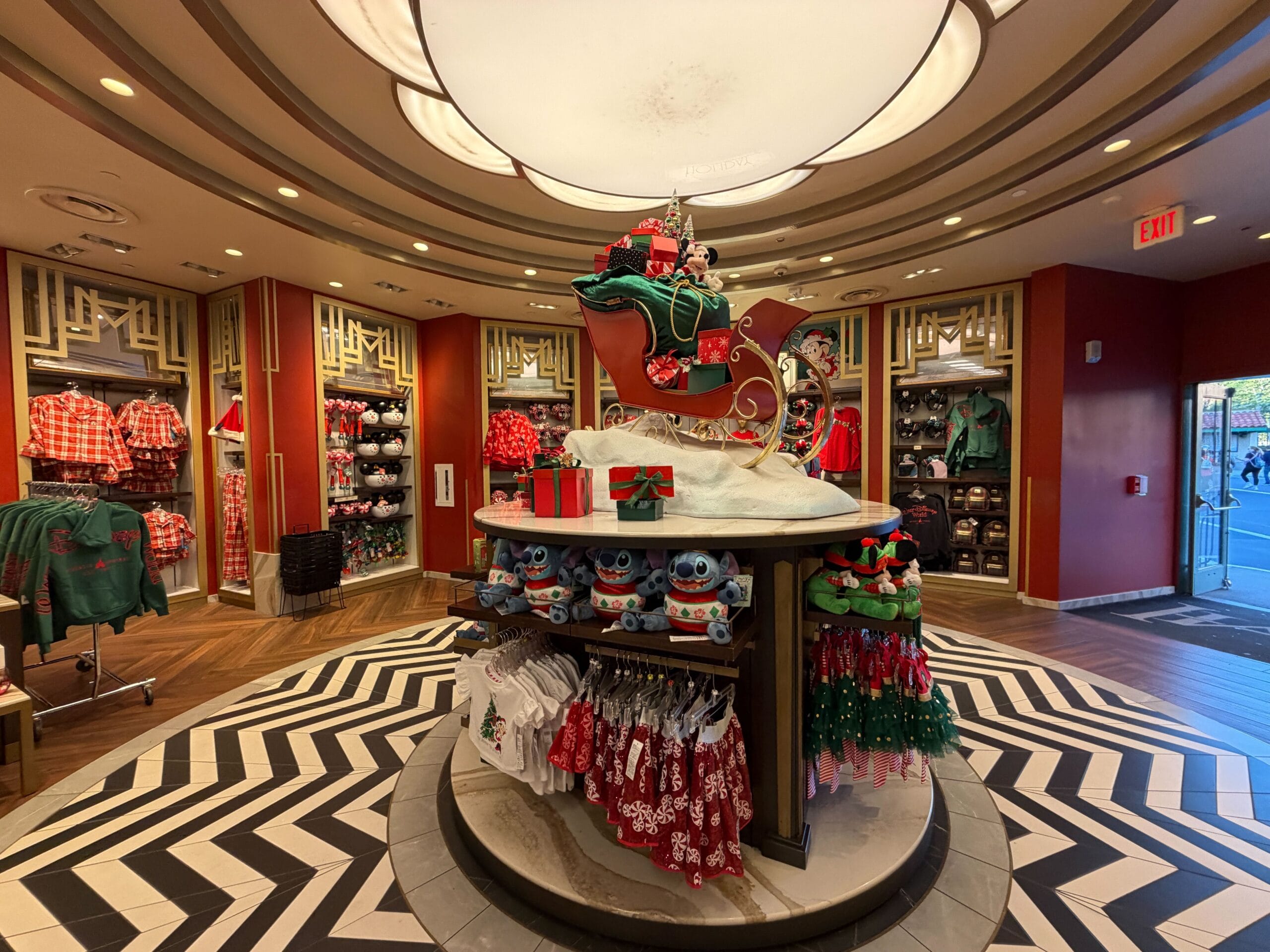 A festive Disney store display features Stitch plushes in Santa hats, gifts, and a sleigh, evoking classic holiday park decor.