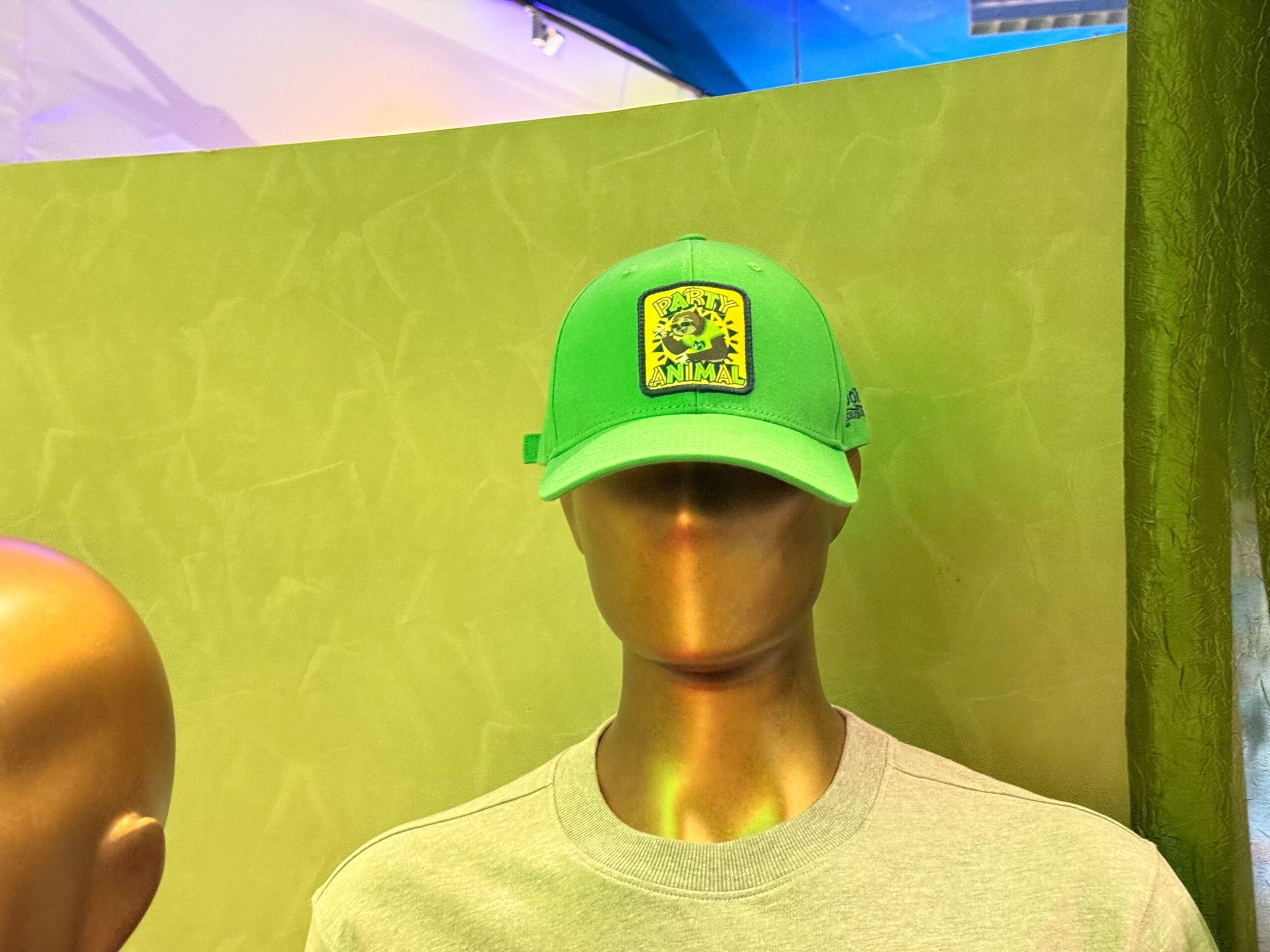 Bronze mannequin in gray shirt and green cap with yellow "Animal" patch, posed before a green backdrop like those at Disney parks.