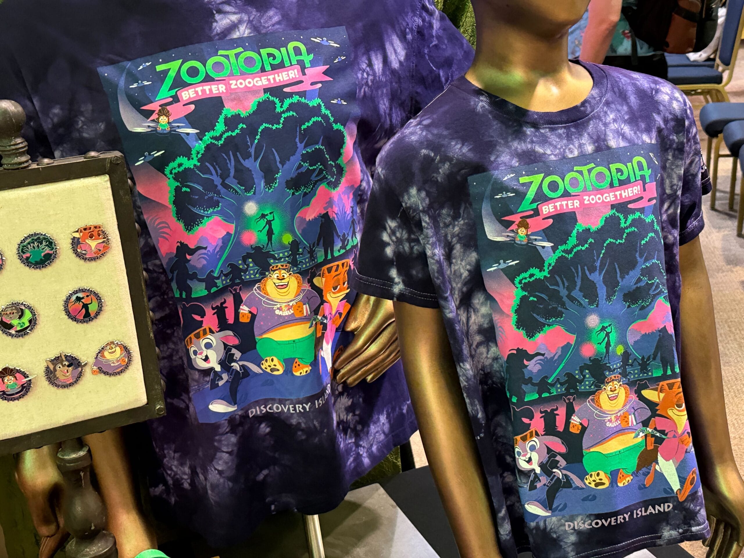 Two colorful tie-dye "Zootopia: Better Zooget'her!" shirts with Discovery Island text, on display at a Disney park store.