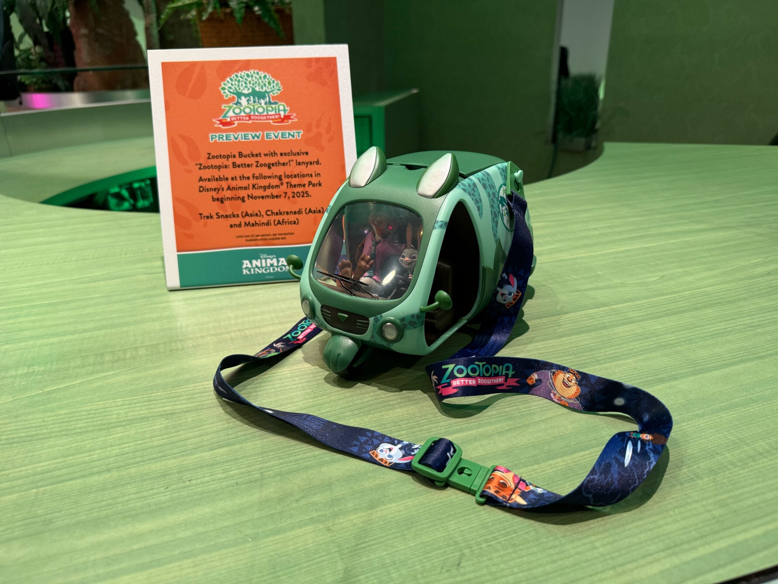 A green Zootopia vehicle bag with a vibrant strap sits beside Zoogether Opening Day Pin merch on a green table, Disney Parks style.