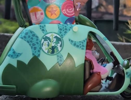 A dinosaur-shaped toy car with animal figures inside sits in front of a colorful Disney’s Animal Kingdom cup, no castles visible.