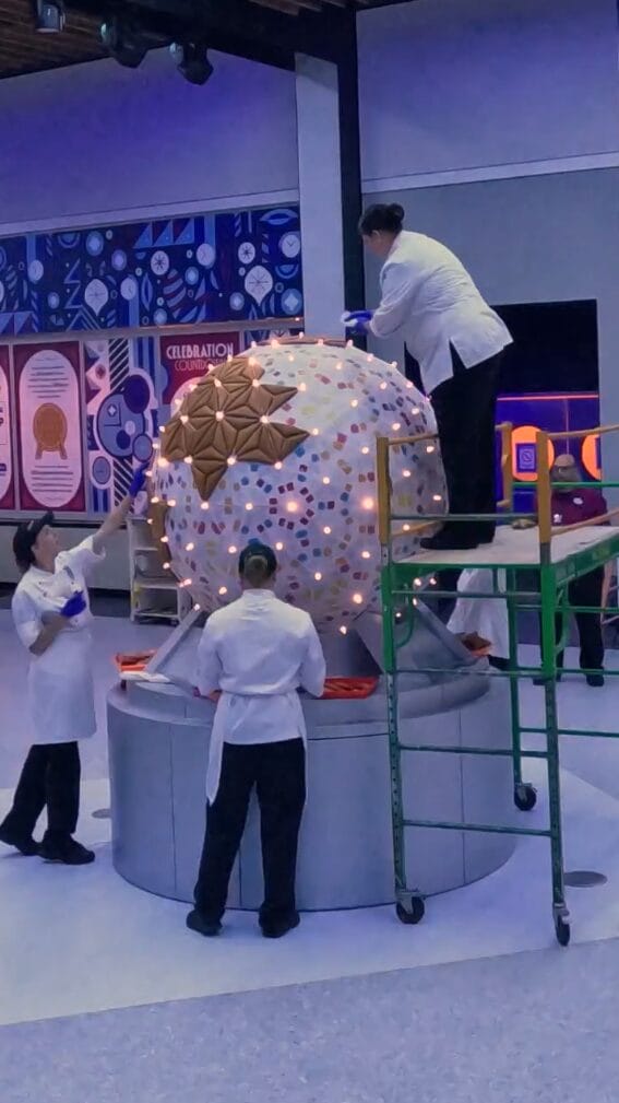 The video shows the team of pastry chefs assembling the display by attaching gingerbread panels to a lighted spherical base.
