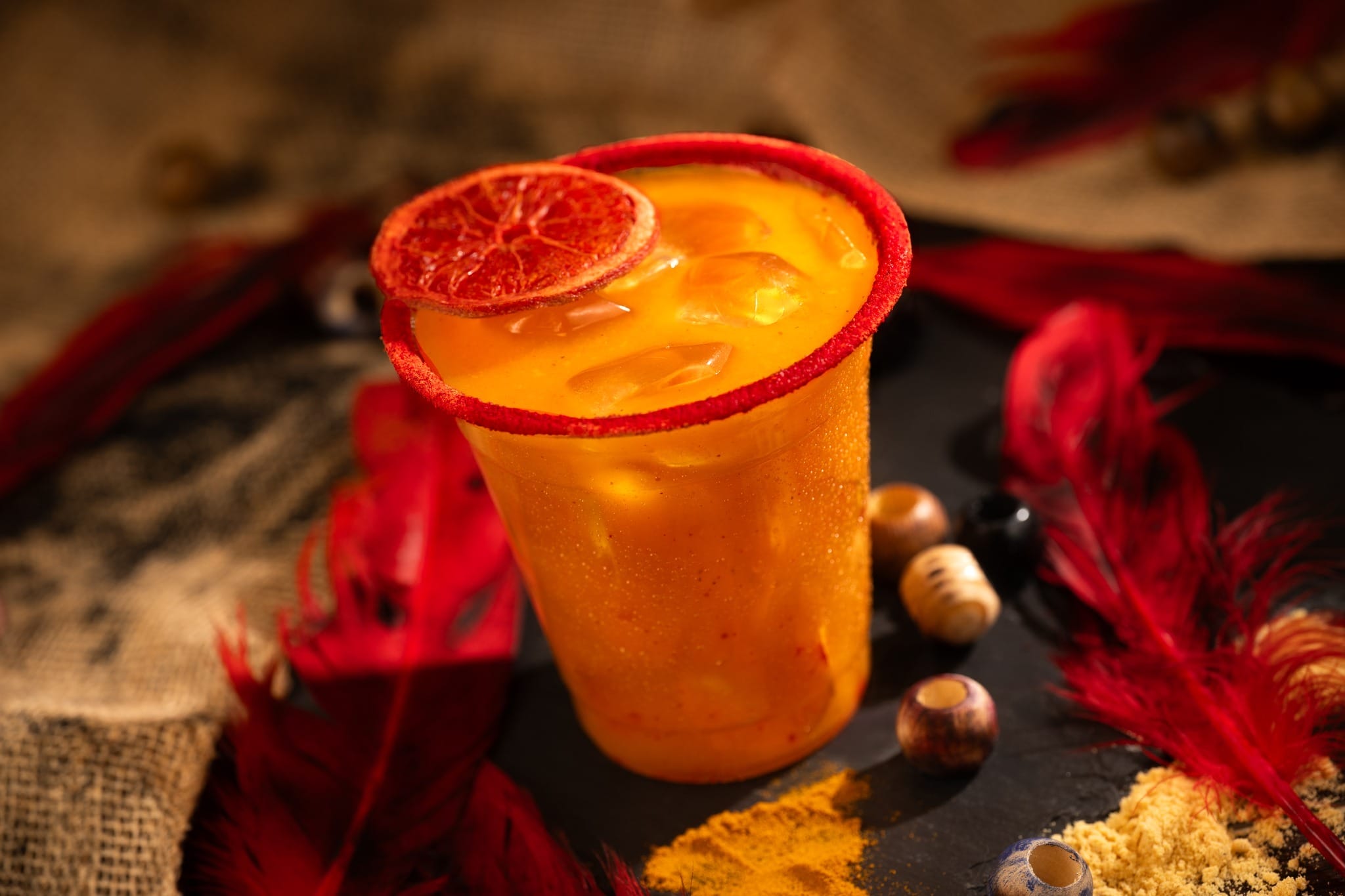 The Trader's Tailwind is made of Captain Morgan Original Spiced Rum, Bols Triple Sec Liqueur, mango purée, Minute Maid Orange Juice, chamoy, and ginger beer with a chili-lime-rimmed glass garnished with a dehydrated blood orange wheel.