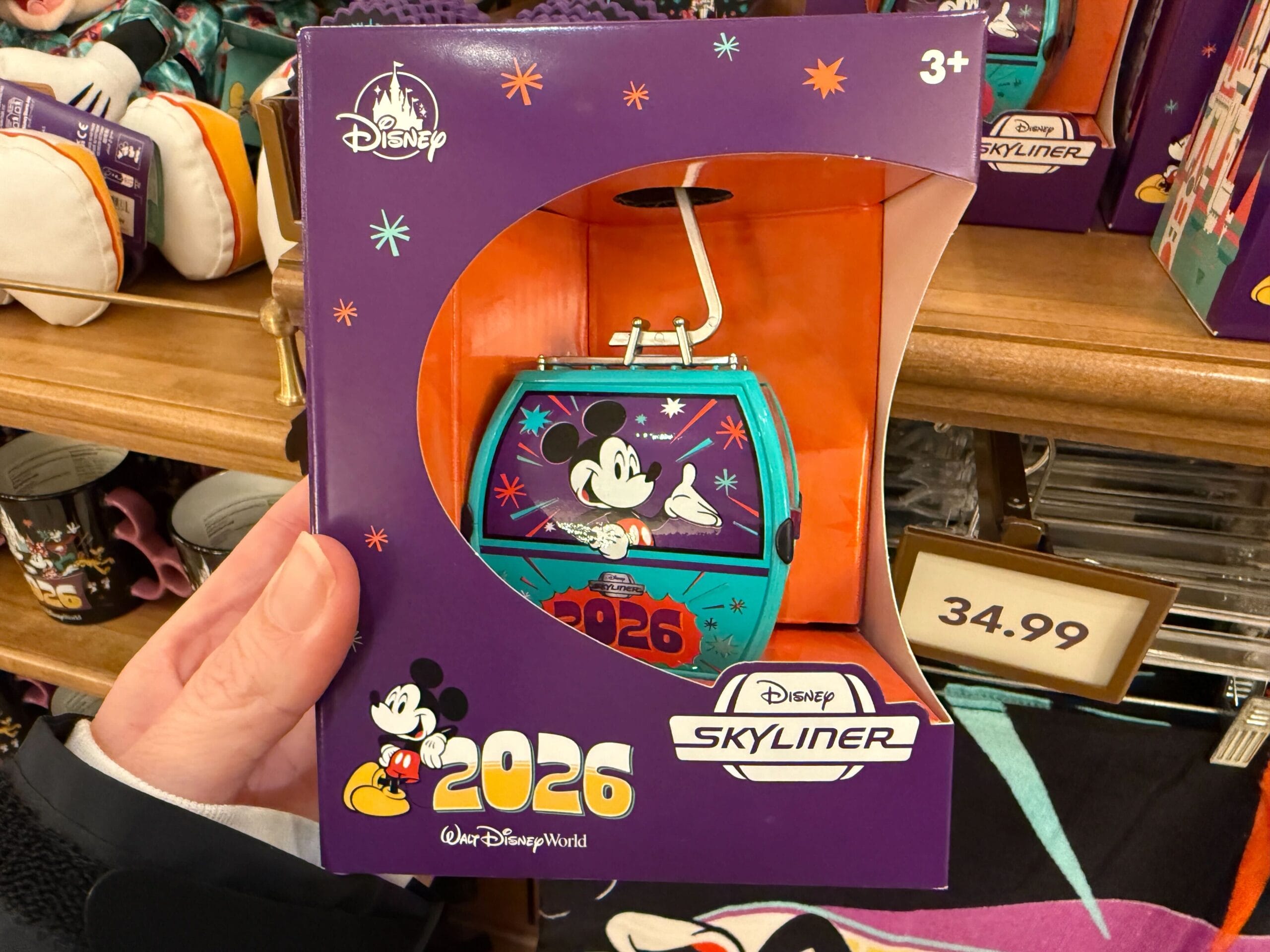 The gondola figure is aqua-colored with purple windows. Mickey is pictured on one window above the year. This includes a display stand.