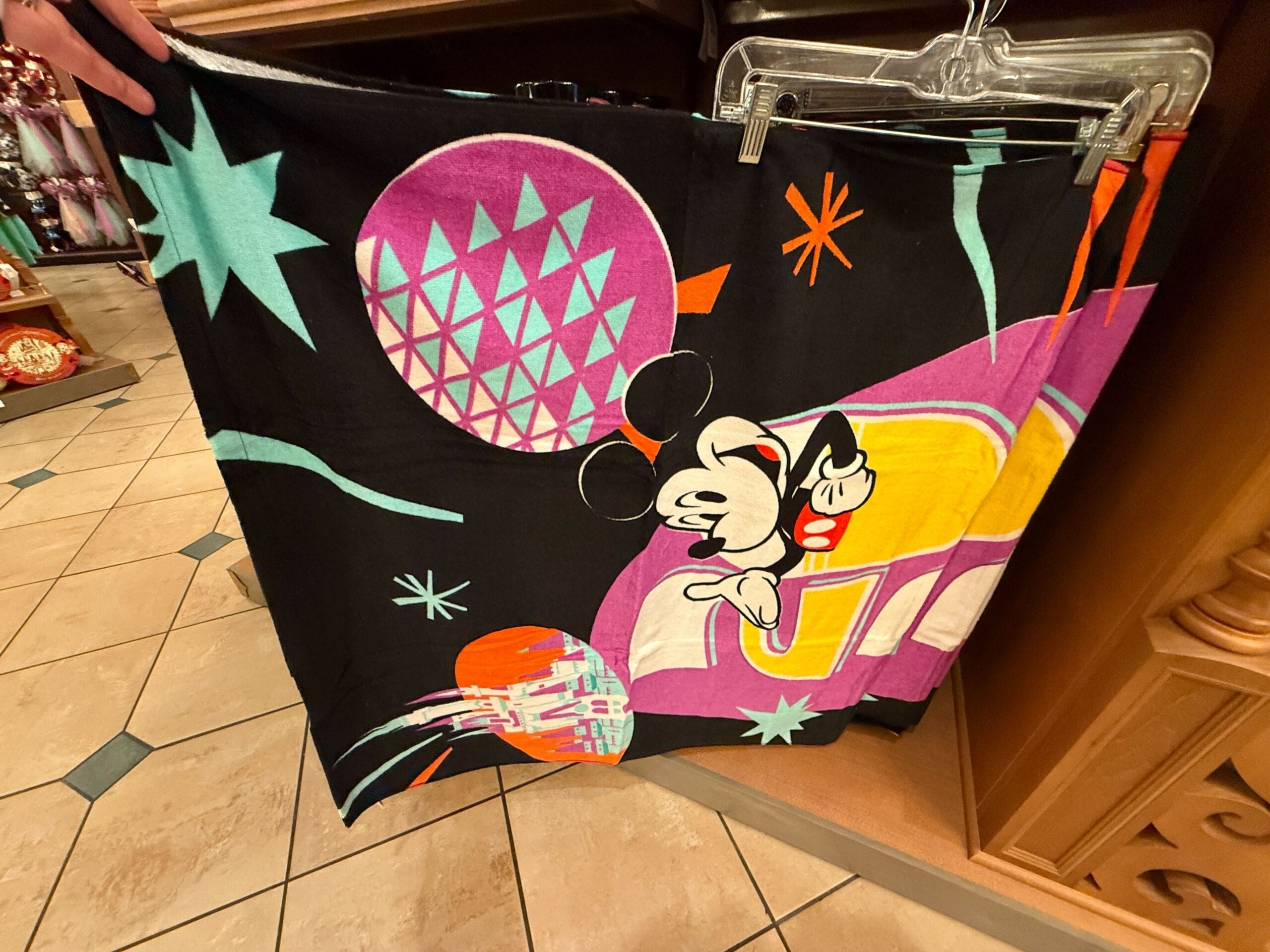 The beach towel is also black with a design featuring Mickey and Friends, park icons, and starbursts all around the year.