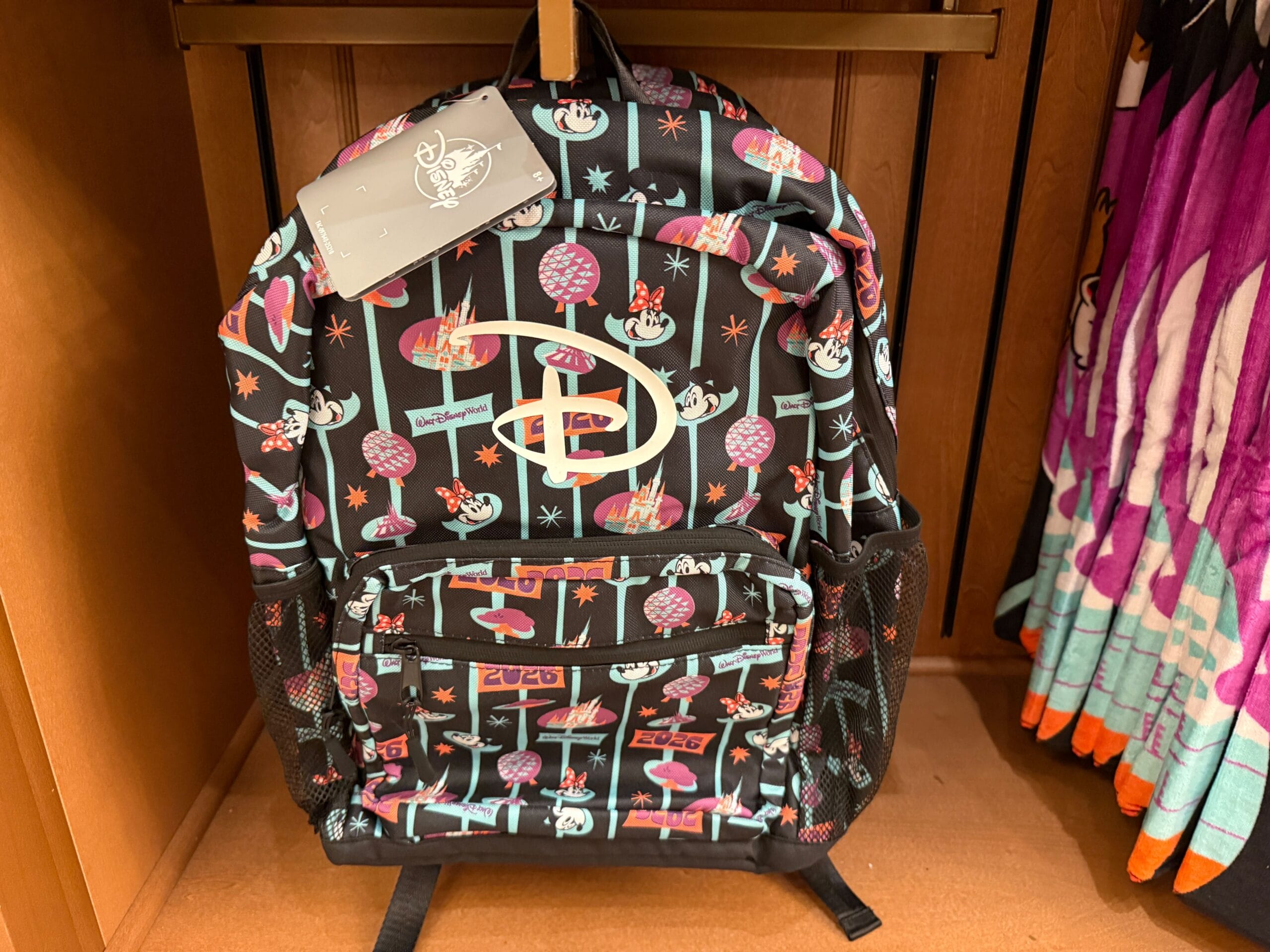 The backpack is black with aqua blue striping. Along the stripes are Mickey and Minnie's faces, "2026", and theme park icons.