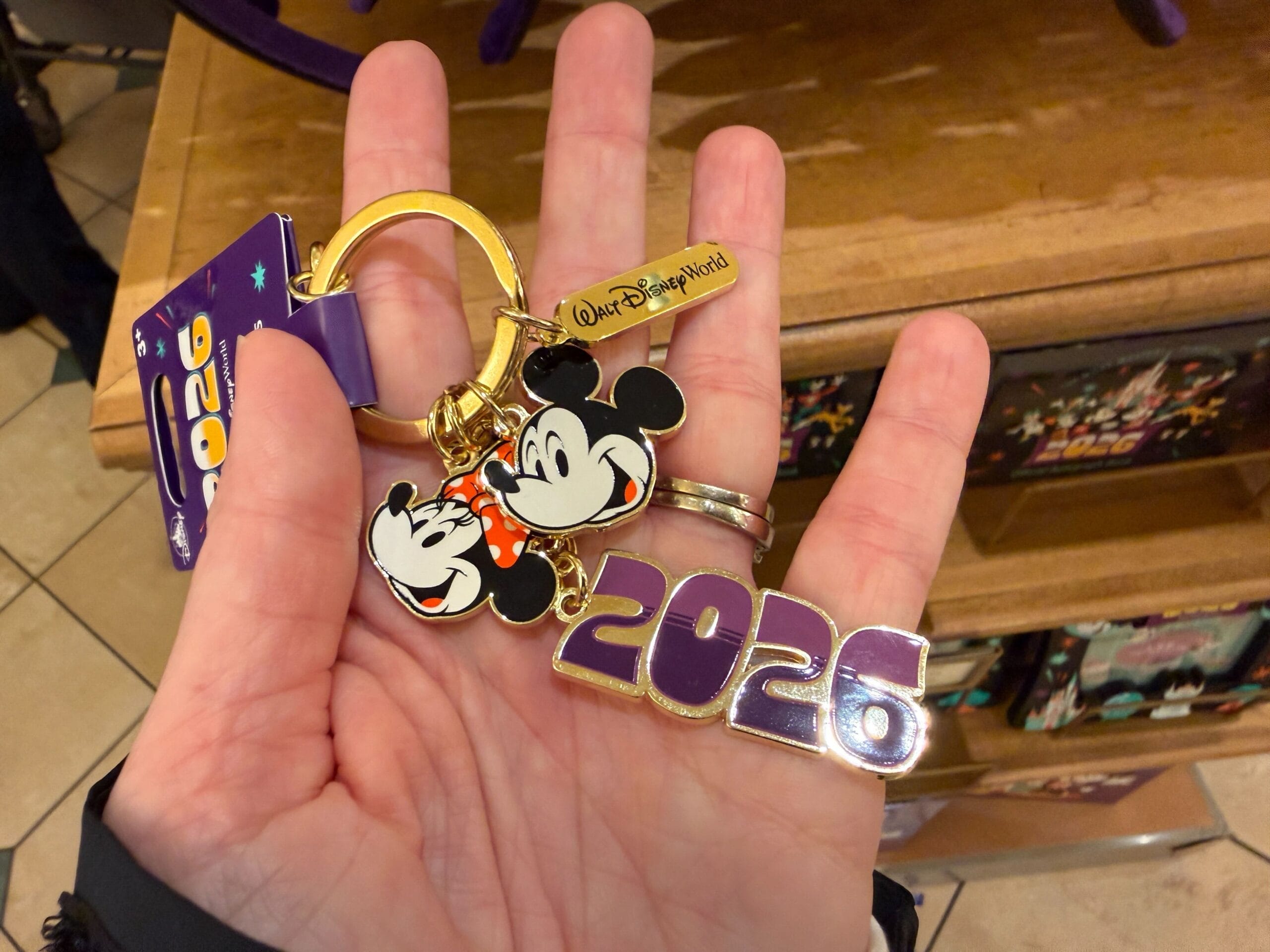The keychain is gold-tone with charms of Mickey, Minnie, the Walt Disney World wordmark, and a big purple "2026."