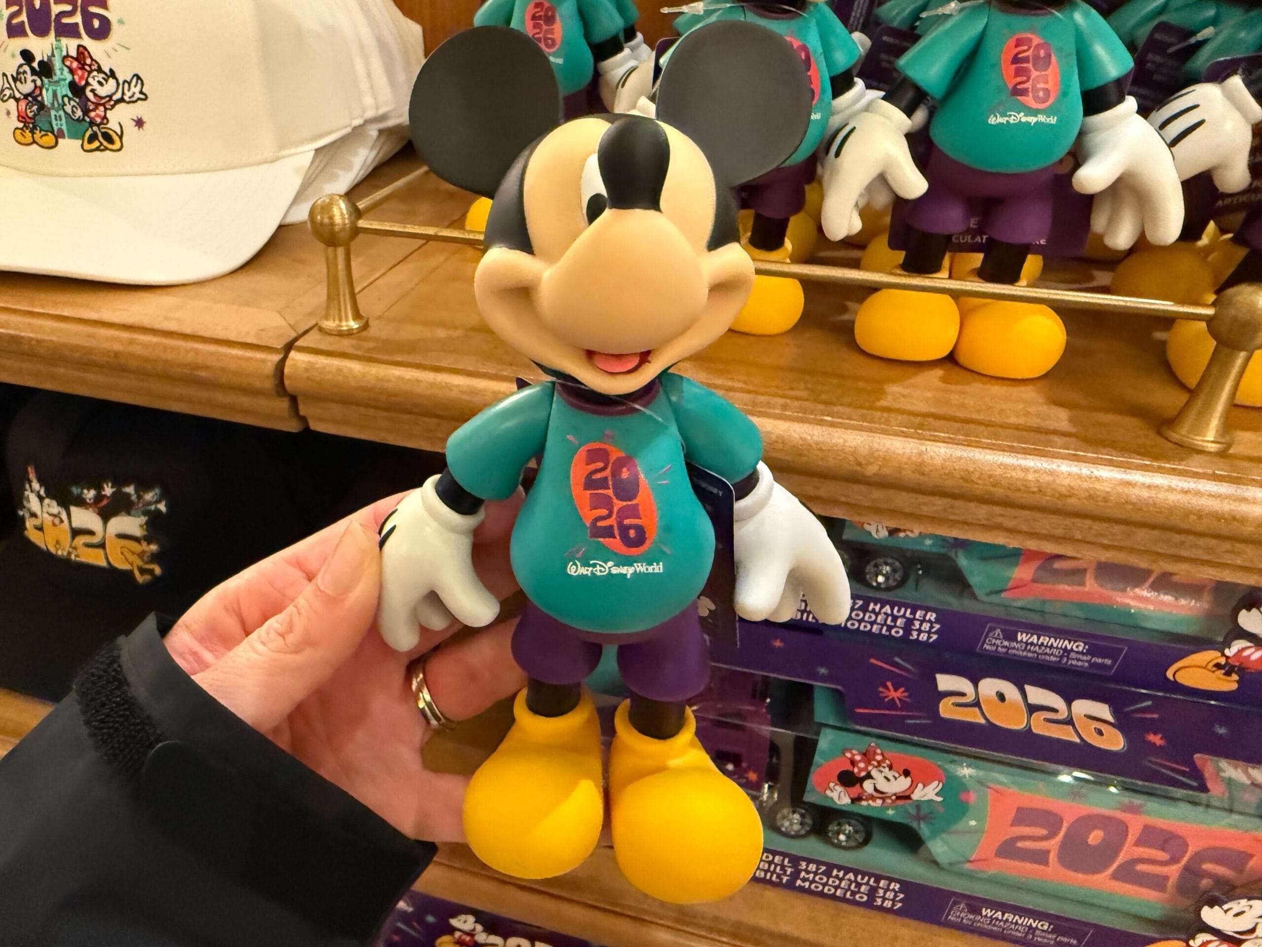 The articulated Mickey figure is plastic with poseable arms. He has a teal "2026" shirt, purple shorts, and yellow shoes.