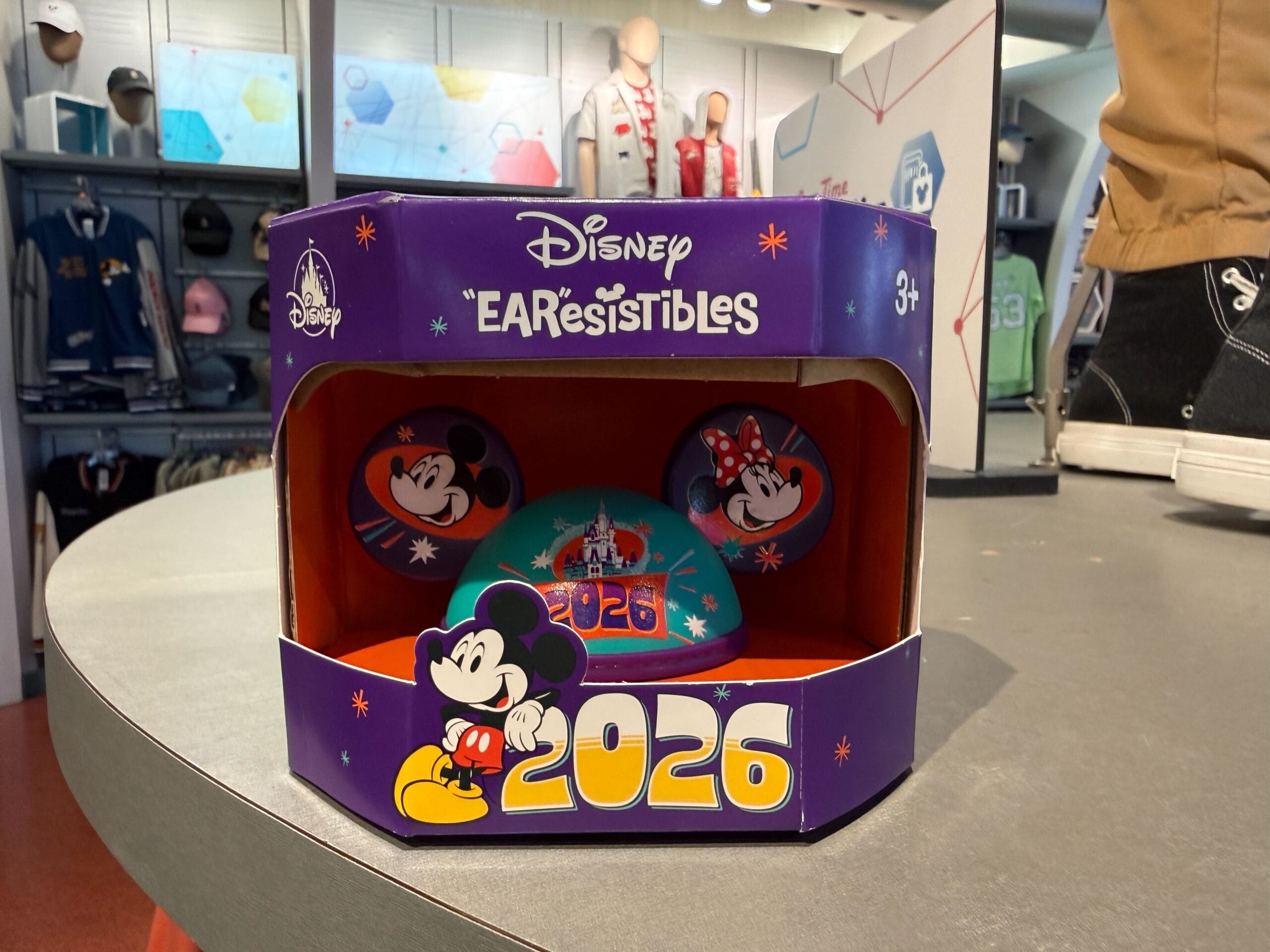 The latest "EAR"esistibles figure has an aqua-colored cap and purple Mickey ears. Mickey and Minnie are pictured on the ears. "2026" and the castle are on the front.