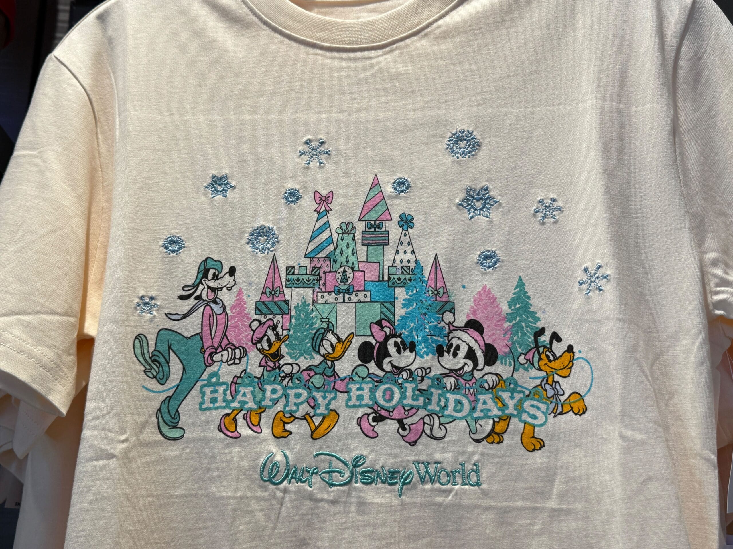Goofy, Daisy, Donald, Minnie, Mickey, and Pluto are dressed in matching winter attire and carrying a letter banner that spells out “Happy Holidays.”