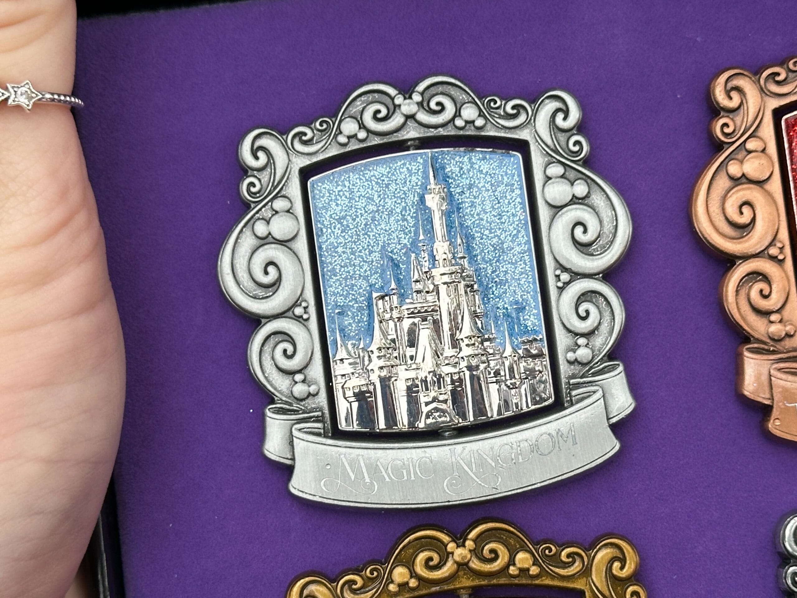 The Magic Kingdom pin has a silver finish with Cinderella Castle pictured against a sparkly blue background.