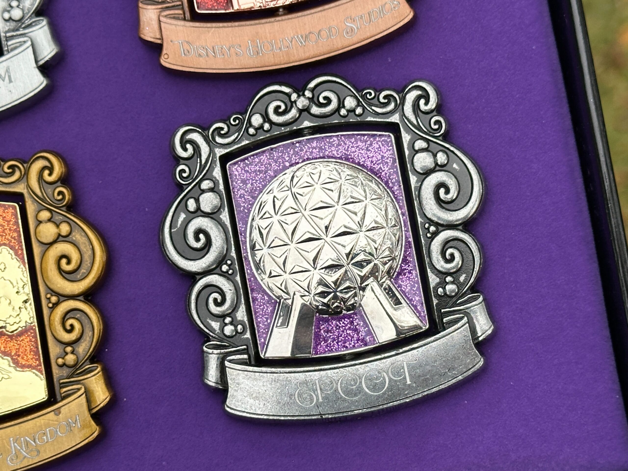 The EPCOT pin is dark silver with Spaceship Earth against a purple sparkly background.