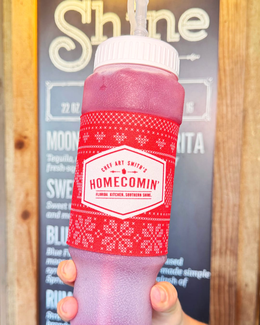 The 24 oz squeeze bottle has a red wrap around the center featuring a fair isle design. It has the Homecomin' logo on one side and "Chicken-Fried Christmas" on the reverse.