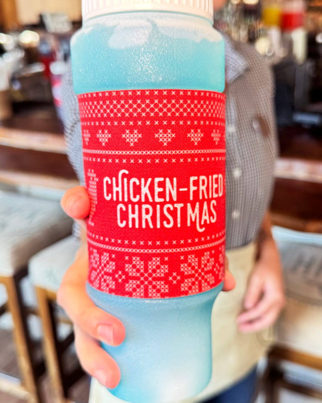 The 24 oz squeeze bottle has a red wrap around the center featuring a fair isle design. It has the Homecomin' logo on one side and "Chicken-Fried Christmas" on the reverse.